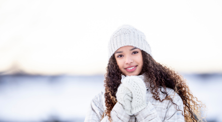 Smiling woman with curly hair wearing a winter hat and mittens in the snow