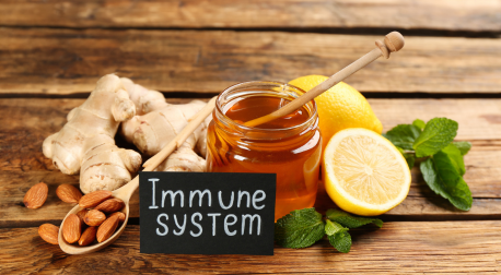 Honey jar, ginger, lemon, almonds, and mint on wood with an immune system sign.