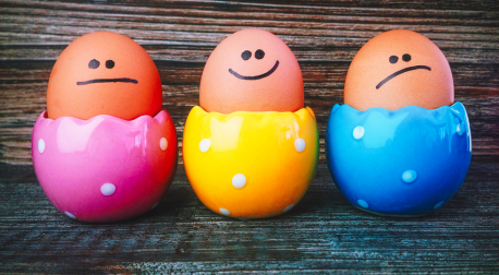 Three brown eggs with drawn-on faces showing different moods in colorful cups