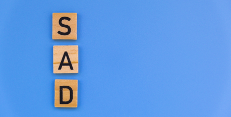 Wooden letter tiles spelling SAD vertically on a bright blue background.