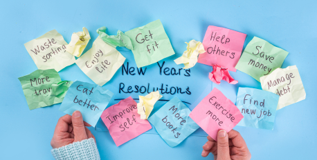 Hands holding colorful sticky notes with handwritten New Year's resolutions on a blue background.