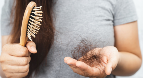 Woman holding a wooden hairbrush and a clump of fallen brown hair in her hand