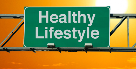 Green highway sign reading Healthy Lifestyle against a bright orange sunset sky.