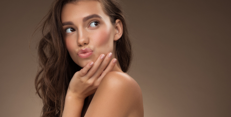 Woman with healthy glowing skin, wavy brown hair, and manicured nails against a warm background.