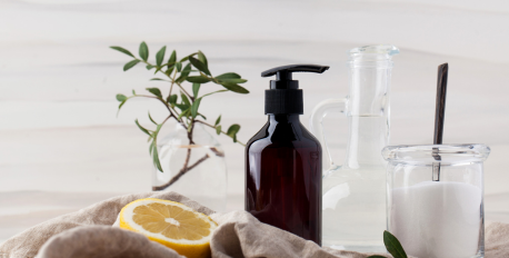 Natural cleaning ingredients including lemon, baking soda, vinegar, and a soap dispenser on a linen cloth.