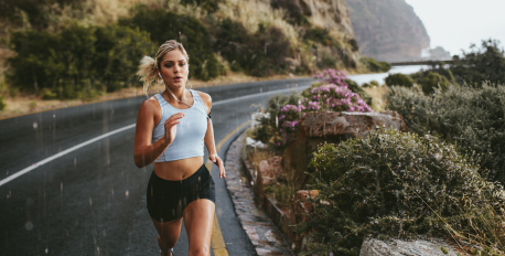 Active woman jogging in light rain on a coastal road, wearing breathable athletic wear.