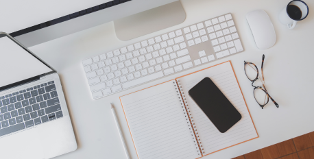 Clean white office desk with a laptop, keyboard, notebook, and glasses.