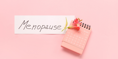Handwritten menopause sign next to a pink calendar and flower on a pink background