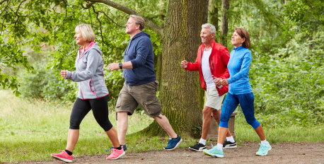 Four active adults power walking together on a trail in a green, wooded park.