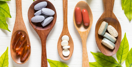 Various dietary supplement capsules and tablets in wooden spoons with green leaves