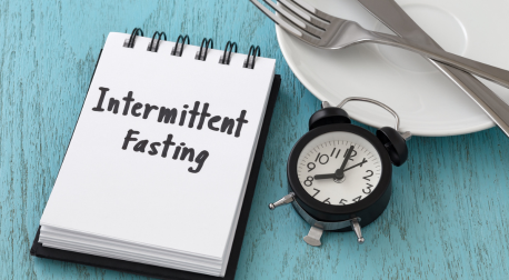 Intermittent Fasting notebook next to an alarm clock and empty plate on a blue wooden table