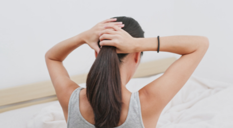 Woman from behind gathering her thick, healthy brown hair into a ponytail.