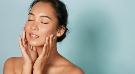 Woman with glowing, hydrated skin touching her face against a blue background
