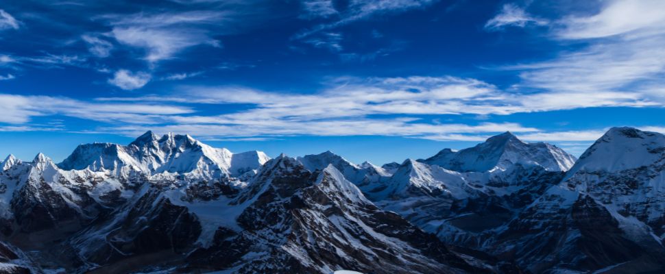 Snow-capped Himalayan mountain peaks under a bright blue sky with wispy clouds