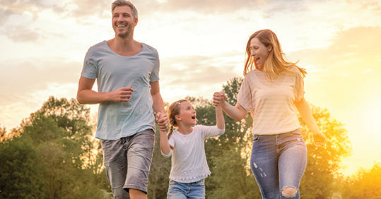 Happy family jogging together outdoors in a sunny park, promoting a healthy lifestyle.