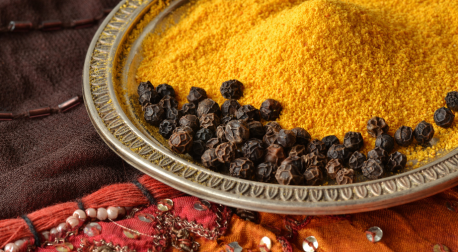 Bright yellow turmeric powder and black peppercorns on a decorative silver plate