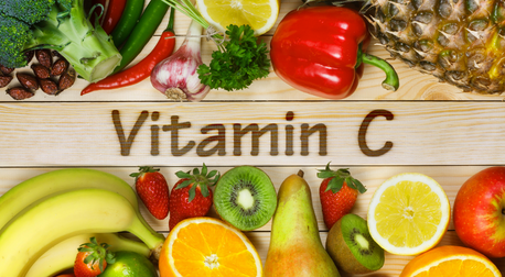 Fresh fruits and vegetables rich in Vitamin C surrounding the text Vitamin C on a wooden background