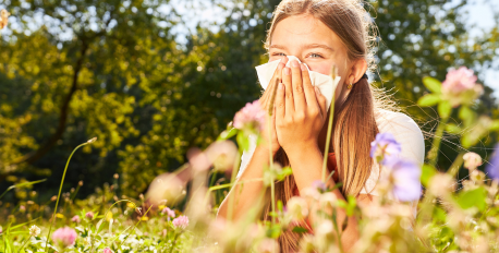 Young girl sneezing into a tissue in a sunny wildflower meadow during pollen season