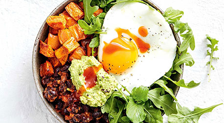 Healthy breakfast bowl with a fried egg, sweet potato, avocado, and fresh arugula.