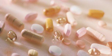 Assorted pastel beauty supplement capsules and pills scattered on a soft pink surface