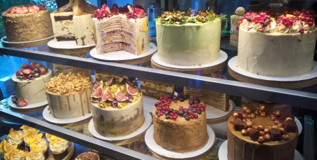 Display case filled with decadent, frosted cakes topped with fresh berries and nuts.
