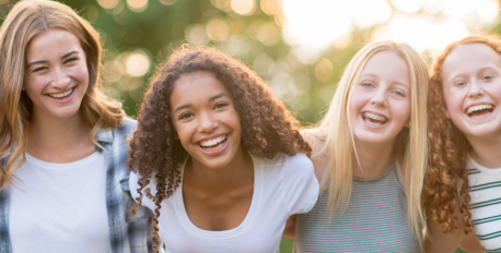 Four smiling teenage girls with clear skin laughing together outdoors in the sunlight