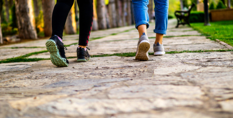 Two people walking side-by-side in sneakers on a stone path in a park.