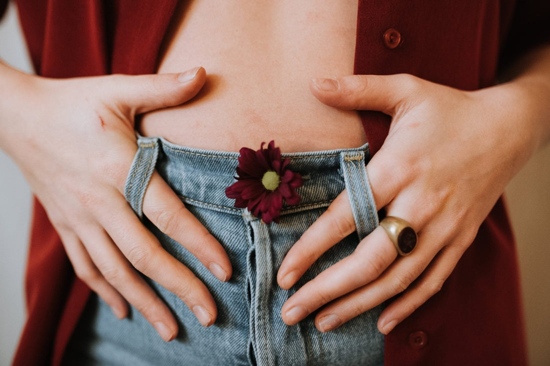 Hands framing a stomach with a small purple flower tucked into blue jeans.