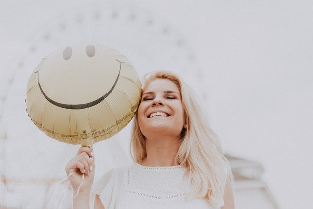 Happy, healthy pregnant woman smiling and holding a yellow smiley face balloon outdoors