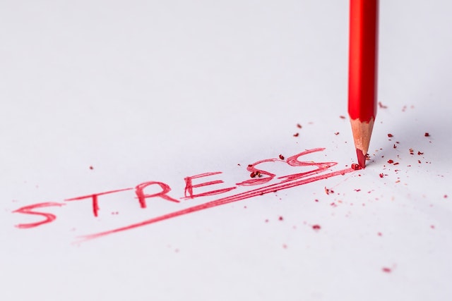 Red pencil with a broken tip writing the word stress on white paper