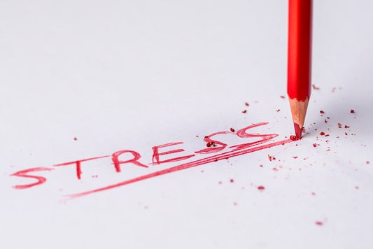 Red pencil with a broken tip writing the word stress on white paper