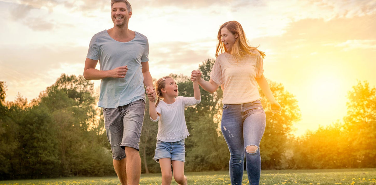 Family of three walking together in a park with a sunset in the background