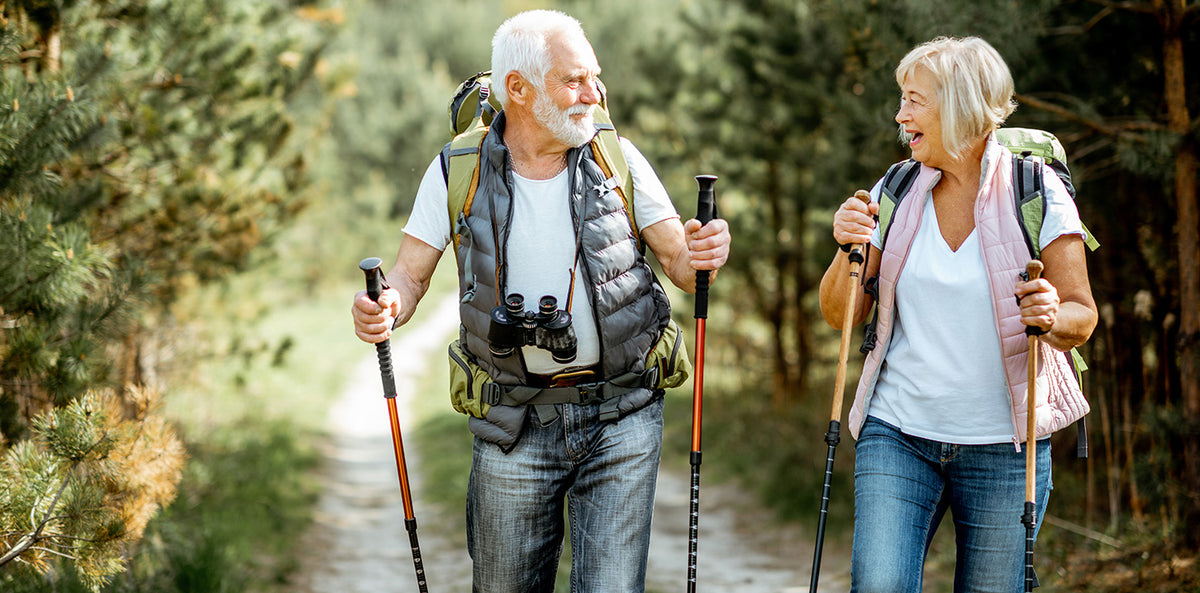 Active senior couple hiking with trekking poles on a sunny forest trail
