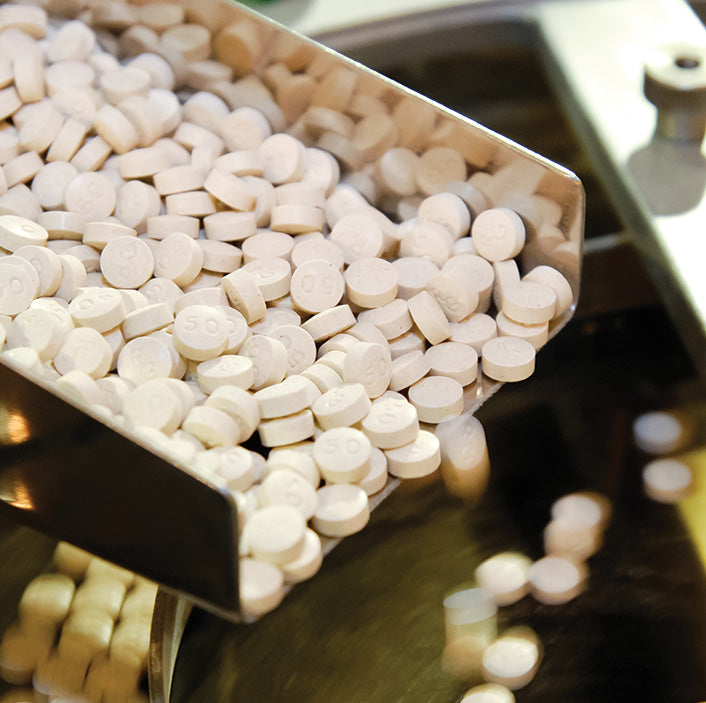 White round pills with embossed numbers on a metal pharmaceutical conveyor belt.