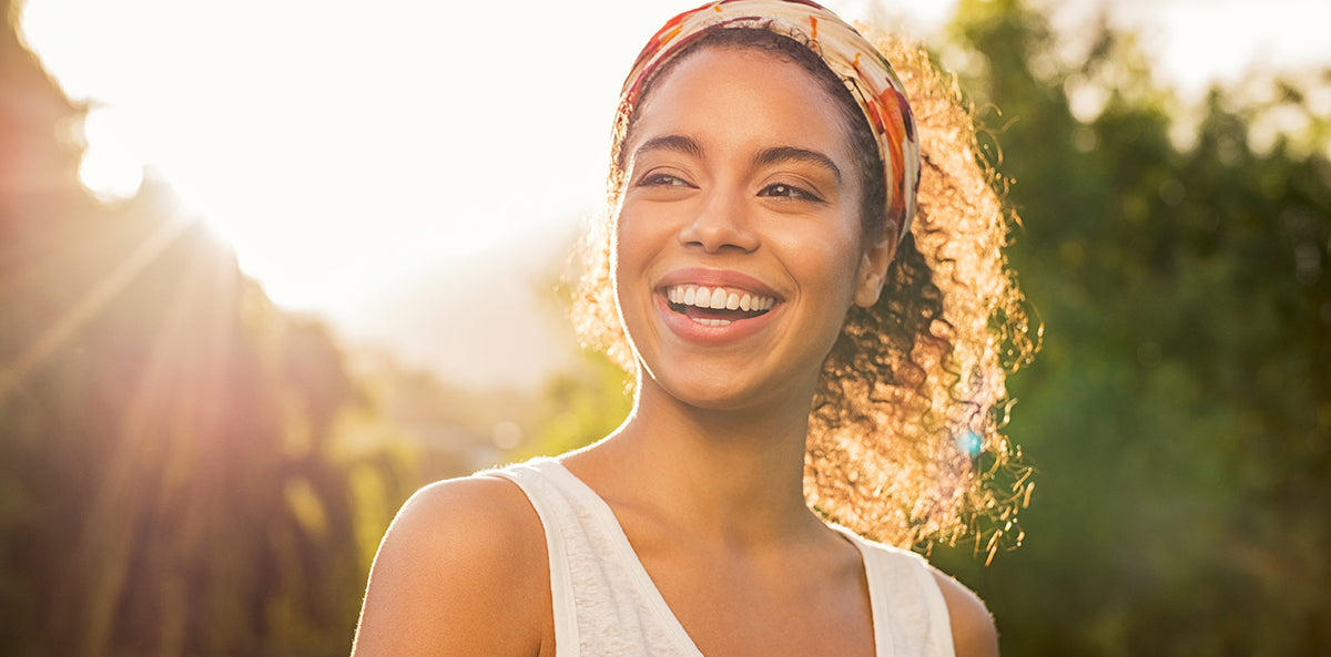Smiling woman with curly hair and a colorful headband in warm, golden sunlight.
