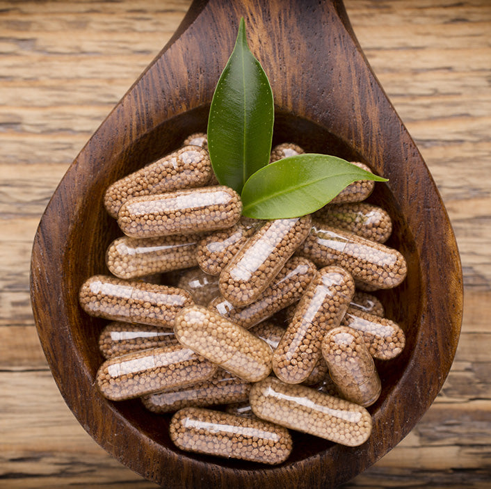 Wooden bowl filled with capsules and green leaves on a wooden background