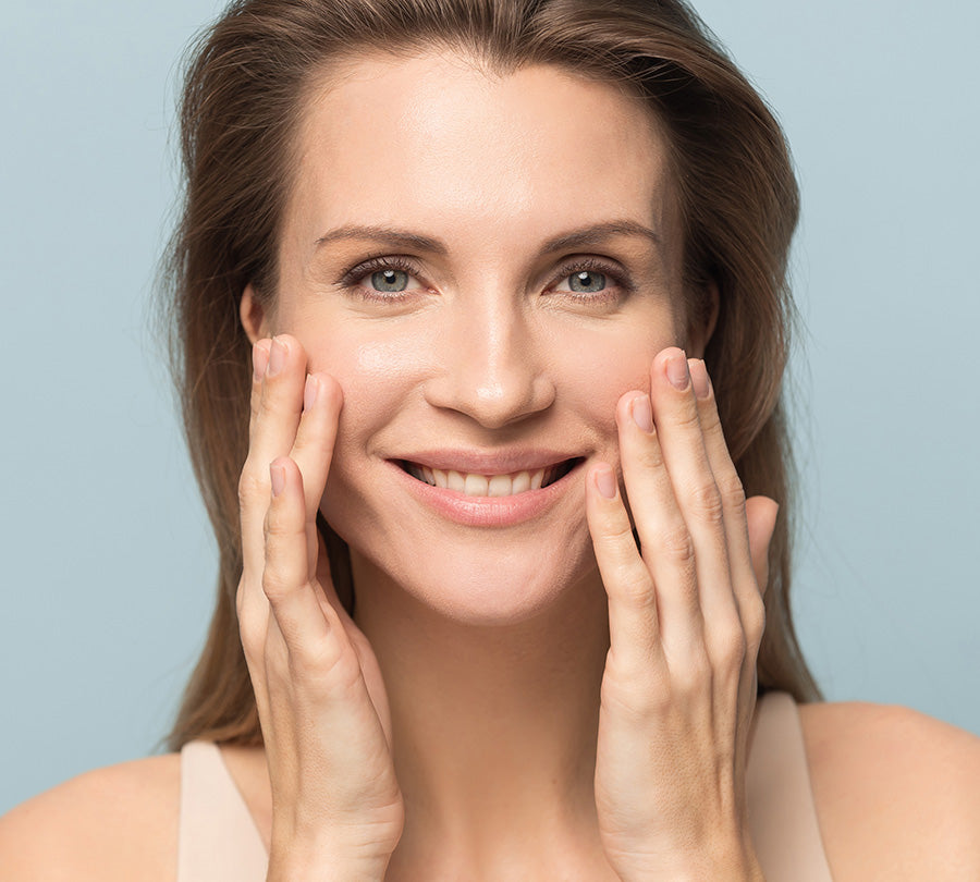 Smiling woman with glowing skin touching her face on a light blue background